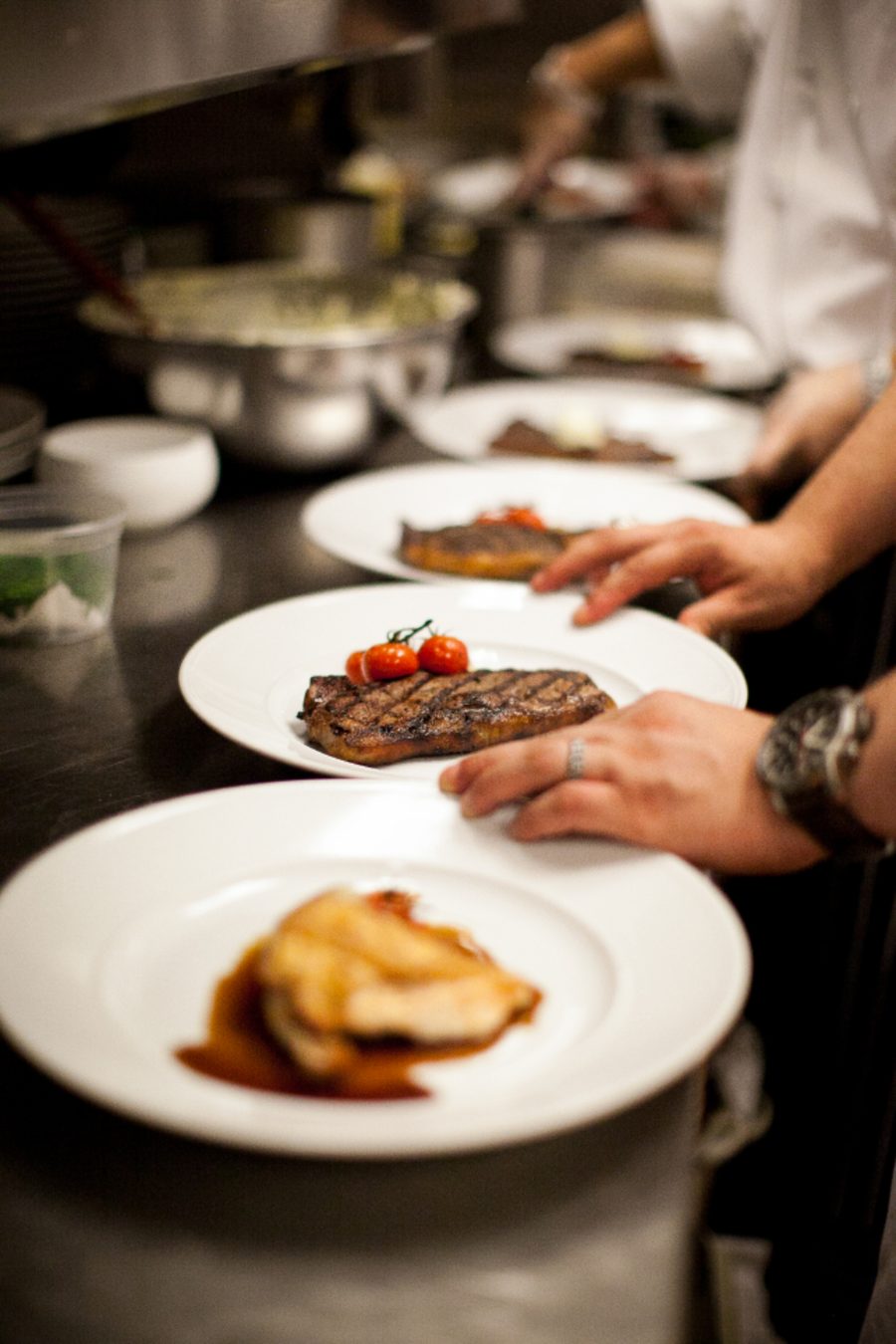 Des assiettes dressées au passe, les mains d'un cuisinier en train de les finir